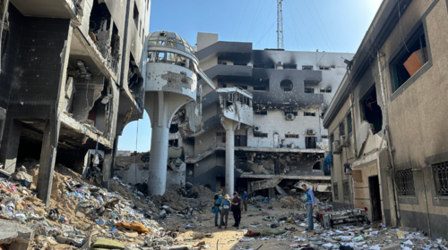 Quatre personnes portant des gilets de l’ONU sont au milieu des ruines d’un bâtiment détruit